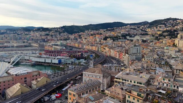 Drone push forward over Genoa&rsquo;s Porto Antico and historic center at sunset, flying over colorful buildings, busy traffic road near harbor.