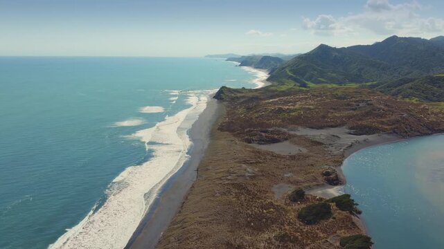 Aerial view of the rugged coastline and Tasman Sea at Marokopa, Waikato, New Zealand. The dramatic landscape features rolling green hills meeting the ocean with waves crashing on the shore.
