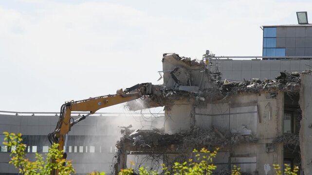 Demolition of reinforced concrete structure, gutting and renovation, hydraulic hammer dismantles building, caterpillar excavator machine at construction site