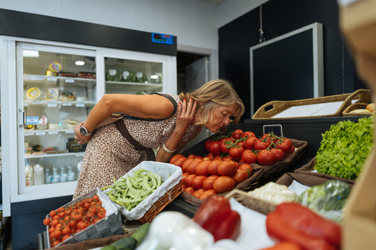 Woman choosing fresh produce by smelling tomatoes in grocery store
