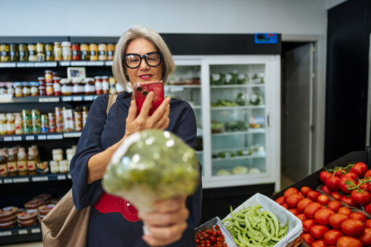 Woman scanning broccoli with smartphone in supermarket aisle