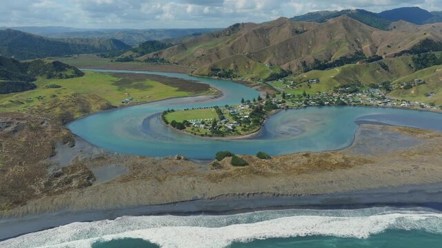 Aerial view of the coastal village of Marokopa, Waikato, New Zealand, nestled between rolling green hills and the turquoise waters of the Tasman Ocean.
