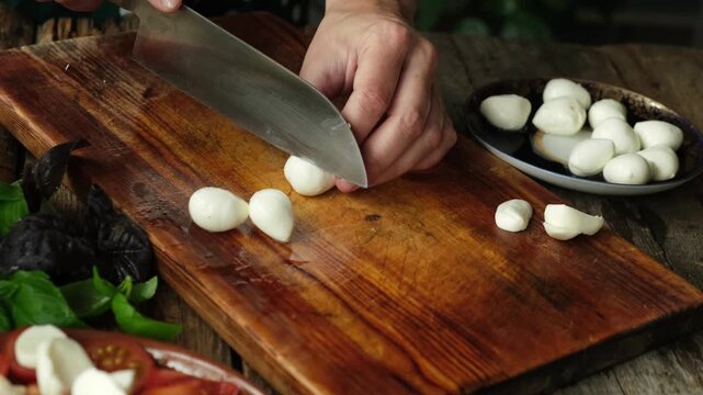 Woman cooking caprese salad. Hands slicing mozzarella cheese on cutting board. Italian cuisine. 