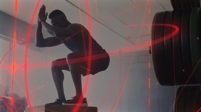 Man swinging arms hopping onto plyobox landing squat training fitness in gym with red swirl overlay