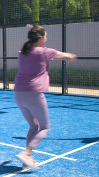 Vertical video: Returning opponent shot, woman in gray tee moving on blue court with paddle