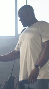 Vertical video: Seeing person, man in tee shifting duffel, glancing at smartwatch at gym to leave