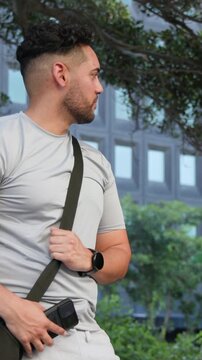 Vertical video: Smiling man in gray tee holding phone, tucking into pouch while watching plaza