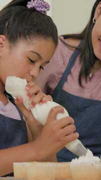 Vertical video: Adjusting piping bag, girl decorating cupcakes at home, denim apron, mom guiding