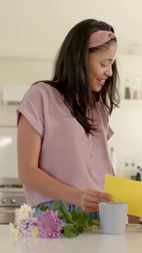 Vertical video: Reading mom in pink top at counter, holding yellow card, as child entering sharing