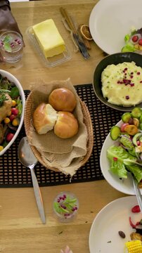 Vertical video: Reaching top-left hand placing roast and bread on home table while guests settling