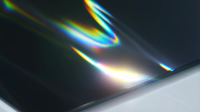 Slow motion tilt pan of light reflections sliding across glossy black surface with rainbow streaks in studio tabletop close up