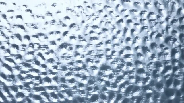 Aerial slow motion top down view of rippling water surface with wind driven wave patterns on open ocean during bright daytime