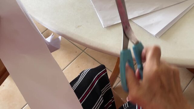 A close up shows hands using scissors to cut white paper into squares to be used as steamer liners for traditional Chinese buns.