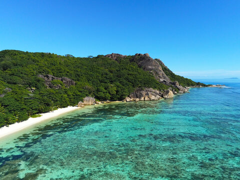 Aerial view of Anse Source d'Argent beach with granite boulders, turquoise coral reefs, and lush tropical forest in L'Union Estate, Seychelles.