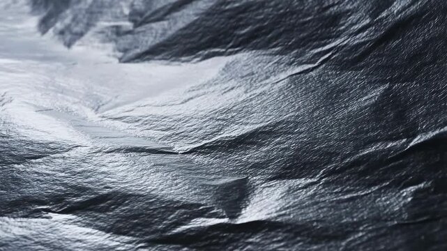 Panning slow motion close up of metallic crumpled foil surface with shifting light reflections on tabletop studio background
