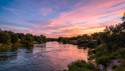 Obraz premium Beautiful river at sunset with pink and orange hues reflecting in the water