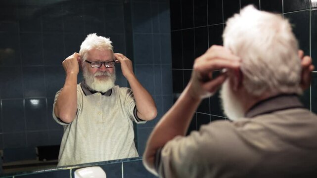 Pension man stands in front of mirror. He ruffle turn his hairstyle into chaos