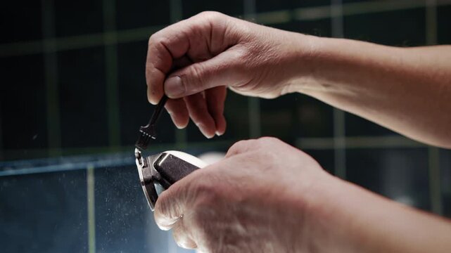 A man hands clean a just used hair clippers with a small brush