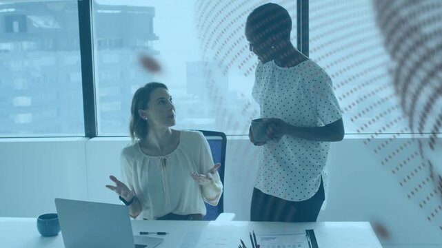 Woman seated pointing at laptop coworker leaning with mug reviewing work charts dot overlay passing