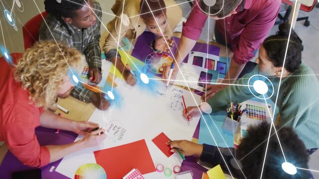 Design team leaning over round table spreading swatches, forming overlay linking nodes across sheet