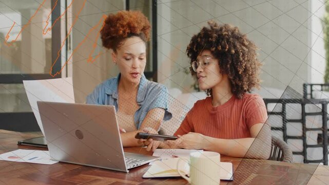 Two coworkers sitting at table right-side woman sliding phone comparing business charts and calling