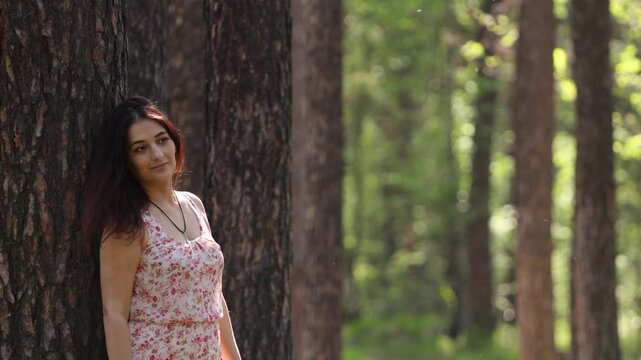 A young woman in a forest. A pretty woman rests in a forest, leaning against a pine tree trunk.