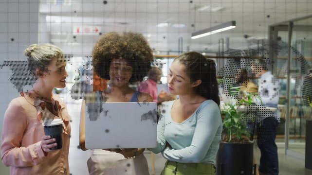 Three women leaning by glass map decal central adjusting laptop others pointing sharing office work