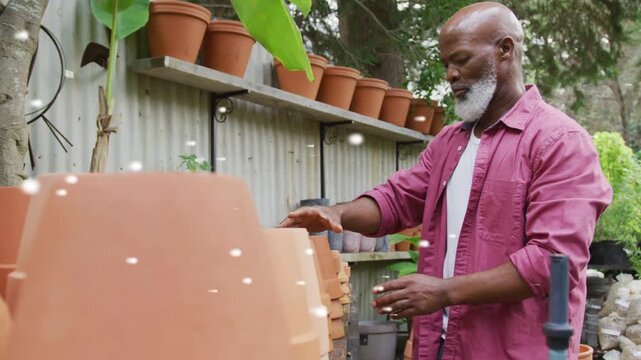 Gardener reaching pots lifting rotating checking rims to stack while flecks drifting across frame