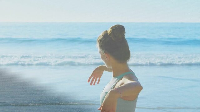 Woman holding bent arms and unfolding into flowing fitness stretch by ocean, light streaks passing