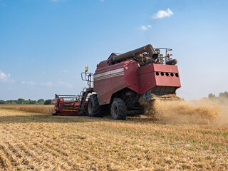 Fototapeta premium A combine harvester working in a vast agricultural field during a sunny daytime harvest, kicking up dust