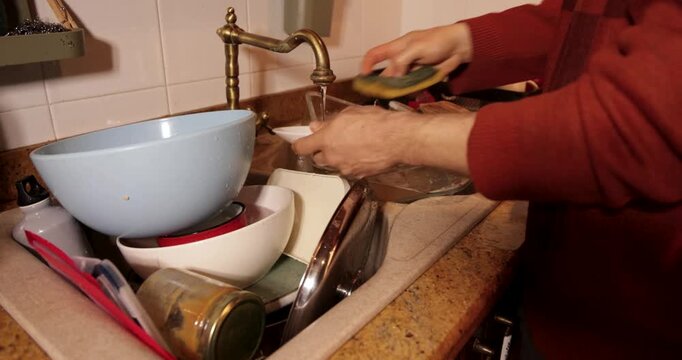 Man washing pile of dirty dishes in kitchen sink