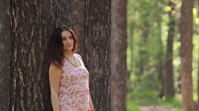 A young woman in a forest. A pretty woman rests in a forest, leaning against a pine tree trunk.