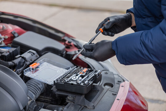 Man repairing car engine using tools under open hood during roadside maintenance