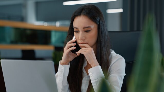 Pensive Caucasian business woman talking phone looking in laptop feeling confused puzzled businesswoman thinking listening client chat talk mobile call using computer tech think female girl in office