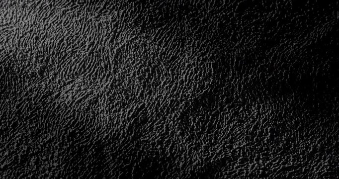 Abstract black texture. The slow, smooth diagonal movement of a dark, rough surface moving in a soft beam of light.