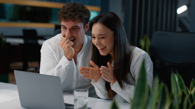 Happy two Caucasian workers business colleagues winning with laptop yelling celebrating win victory achieve businesspeople excited businessman with businesswoman yell rejoice professionals in office