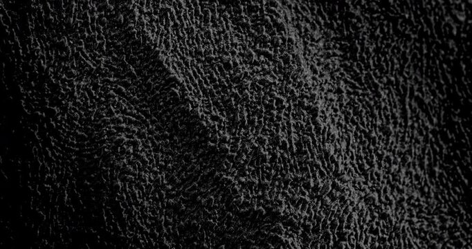 Abstract black texture. The slow, smooth diagonal movement of a dark, rough surface moving in a soft beam of light.