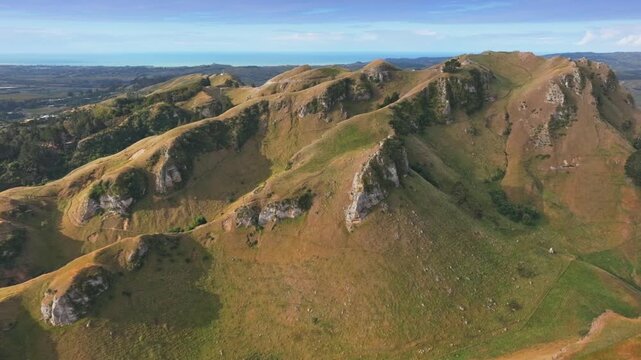 Rolling hills and valleys with rocky outcrops near the coast in Te Mata Peak, Havelock North, Hawkes Bay, New Zealand. The landscape is bathed in golden afternoon light.