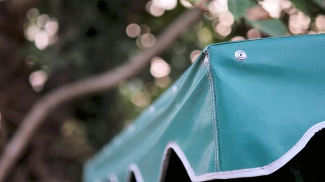 Close-up of a green tarp corner with visible stitching and metal rivets, set against a blurred outdoor background, highlighting material texture and durability.