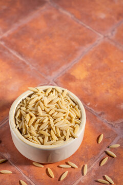 Uncooked orzo pasta in a white ceramic bowl on a tile surface 