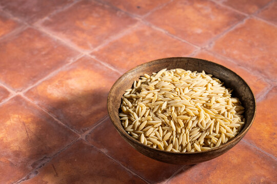 Uncooked orzo in a wood bowl on a tile surface 