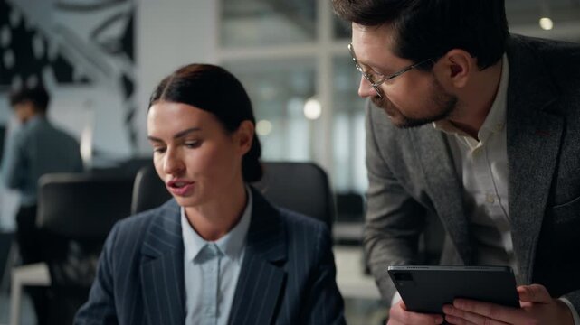 Two Caucasian business partners working teamwork discussing stats using digital tablet and computer businesswoman intern talk with businessman boss mentor talking work partnership office cooperation