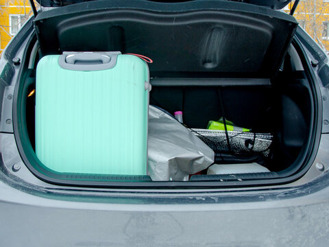 Mint green suitcase and bags packed in open car trunk with autumn background. Road trip preparation, vacation packing, luggage transport, automotive travel concept.