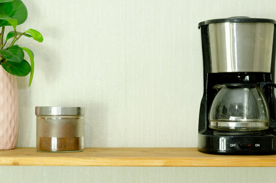 Glass jar with coffee, black drip coffee maker, and potted plant on wooden shelf in kitchen interior. Morning routine, beverage preparation, home decor, and coffee break concept for lifestyle design