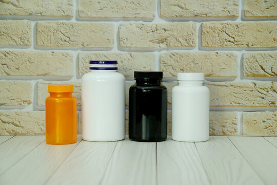 Four medicine bottles in orange, white, and black standing on a white wooden table against a brick wall. Pharmaceutical products, healthcare, vitamins, and medical treatment concept illustration.