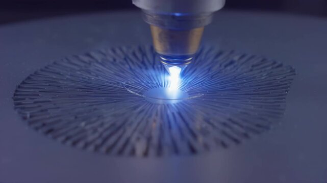 Laser cutting process with focused blue light beam creating intricate patterns on metal surface, showcasing precision and technology in industrial manufacturing setting