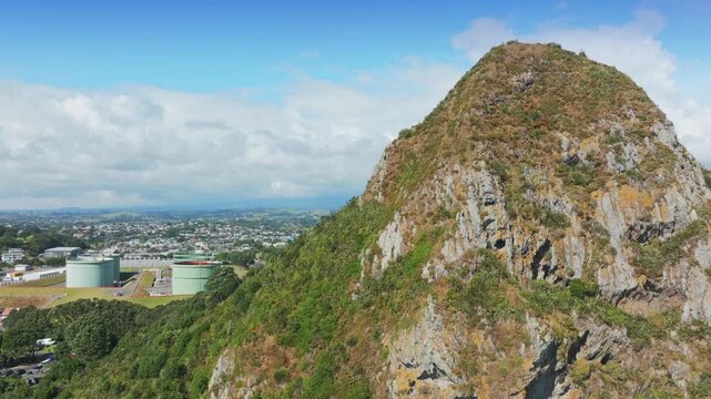 A scenic view of Paritutu Rock, New Plymouth, Taranaki, New Zealand, showcasing its rugged slopes and lush vegetation against a clear blue sky.