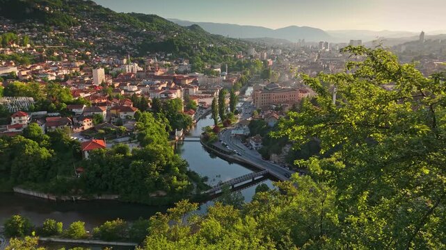 Aerial shot shows the city center of Sarajevo, Bosnia and Herzegovina in a valley. Mountains surround the mix of Ottoman and modern architecture in Sarajevo, Bosnia and Herzegovina