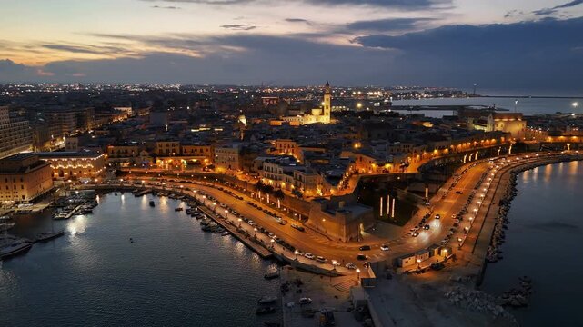 Aerial drone view of city lights illuminating the coastal town of Bari, Italy at twilight. Historic buildings and the harbor sit along the Adriatic Sea in Bari, Italy