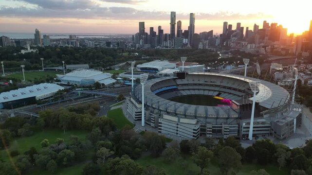 An aerial view of the Melbourne Cricket Ground (MCG) at sunset in front of the Melbourne City Skyline
